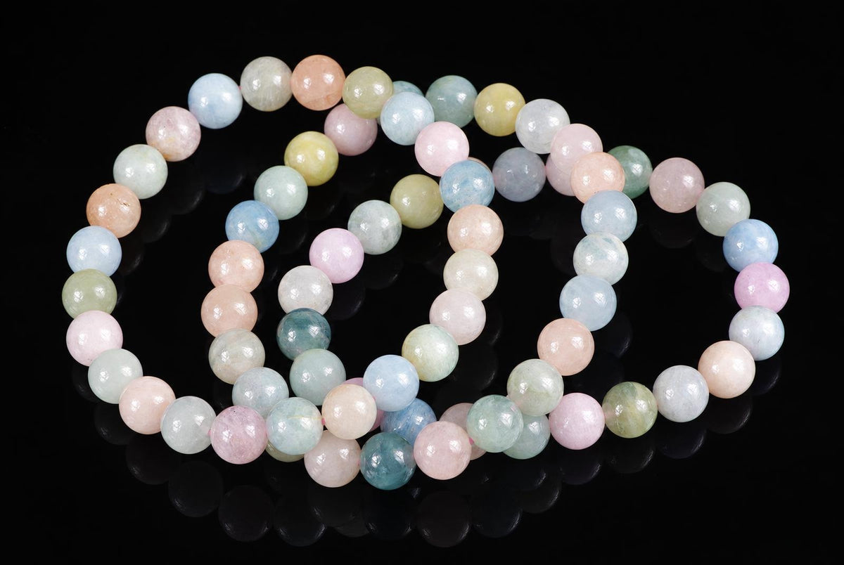 A beryl bracelet with round beads in pastel pink, blue, green and yellow on a dark reflective surface.
