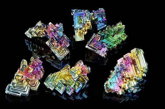 Several iridescent bismuth crystals with rainbow hues arranged on a dark, reflective surface.