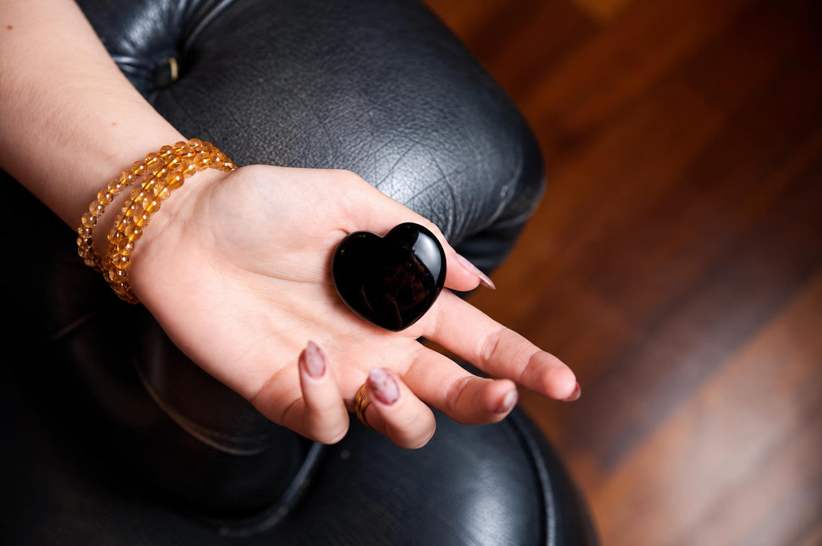 A hand holds a polished black onyx heart against a softly blurred background.
