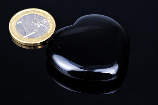 A polished black heart-shaped stone sits on a dark surface next to a one-euro coin.