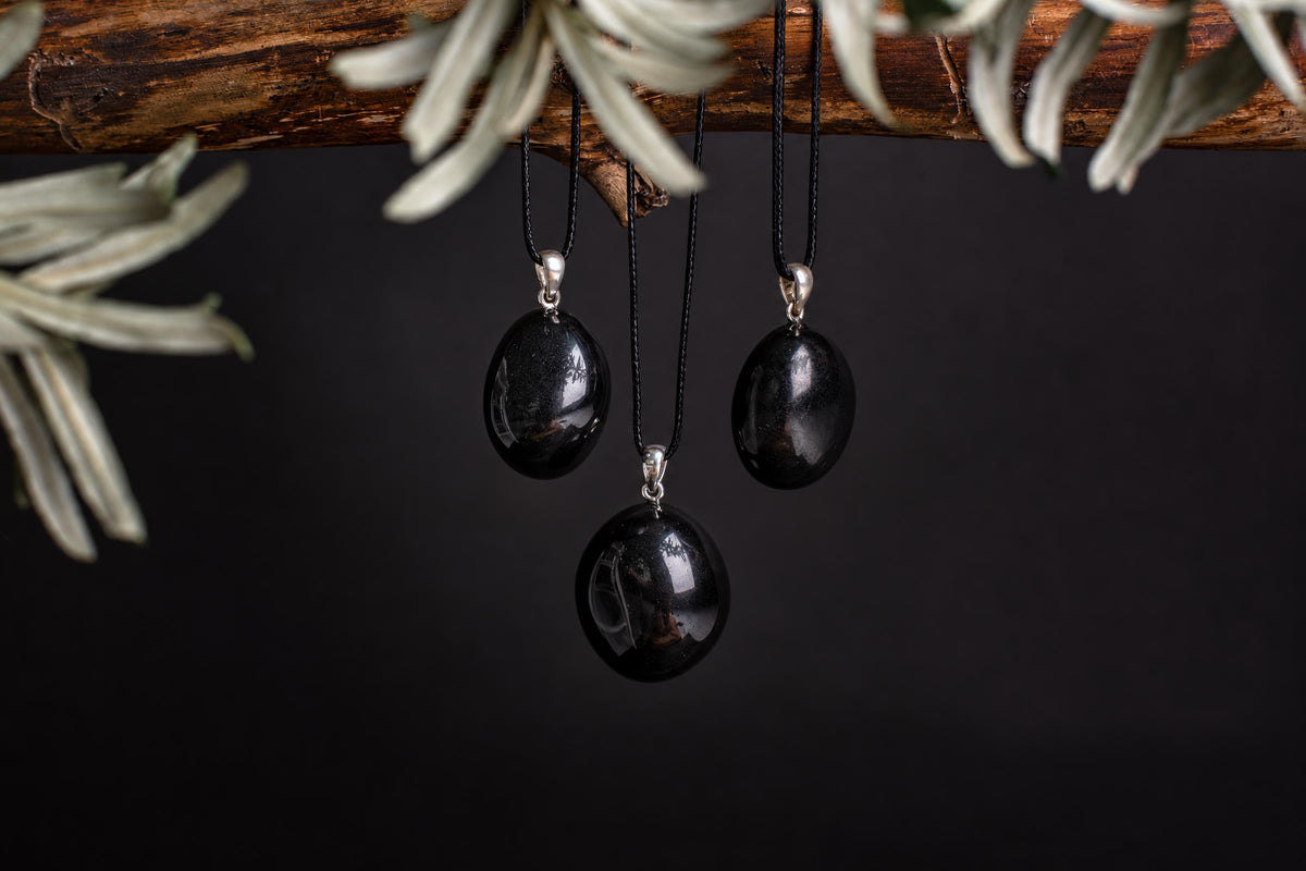 Oval black onyx pendants hang from dark cords beneath a branch with pale leaves.