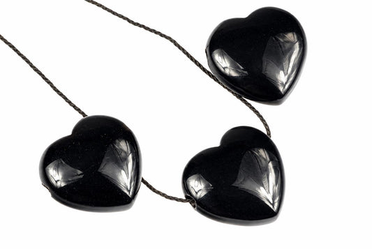 Glossy black heart-shaped onyx pendants are arranged with thin dark cords against a white background, with bright reflections across their curved surfaces.