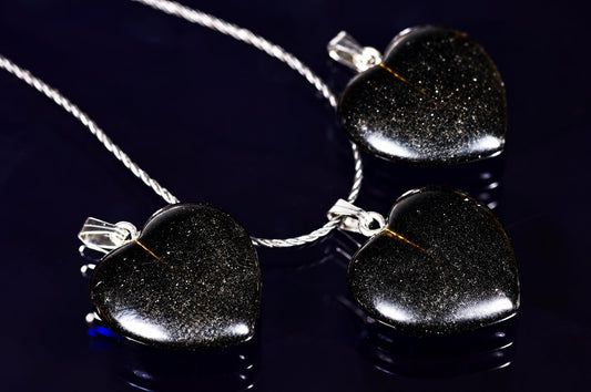 Three heart-shaped pendants with black, glittering stones on silver-toned chains rest on a dark surface.