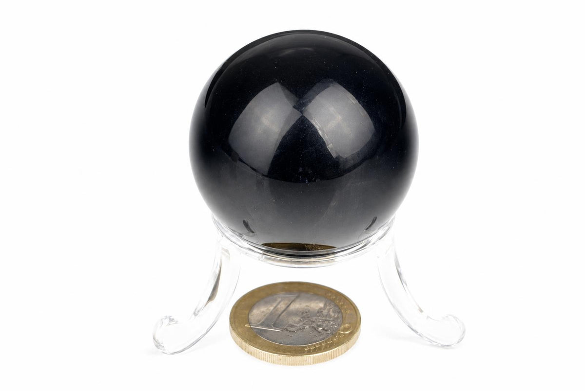 A black sphere on a clear stand with a euro coin for scale, set against a white background.