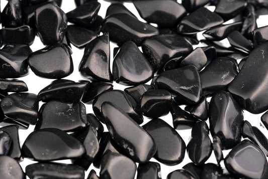 A pile of small, smooth, black stones with a glossy finish scattered on a white surface.