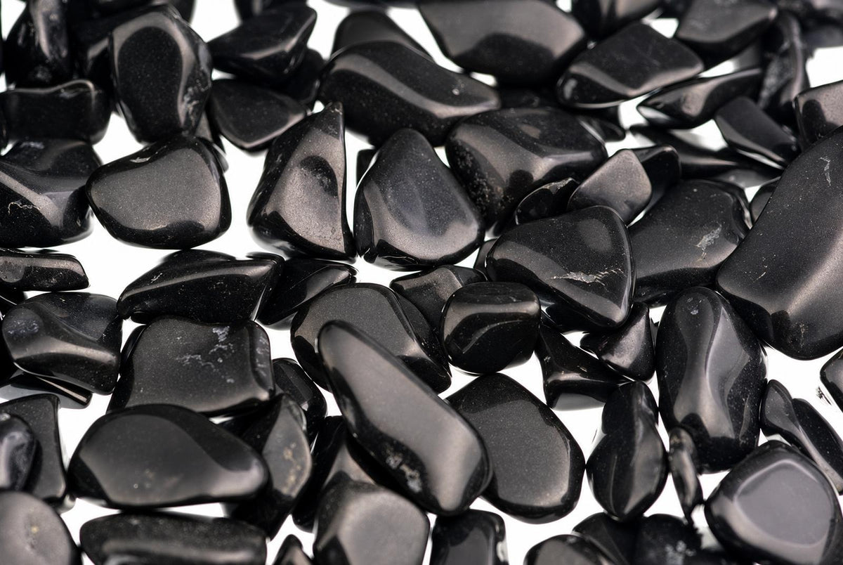 A pile of small, smooth, black stones with a glossy finish scattered on a white surface.