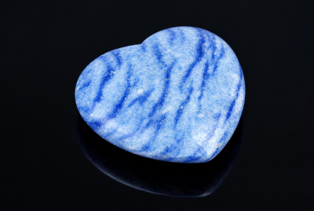 A polished heart-shaped stone with blue and white wavy stripes on a dark, reflective surface.