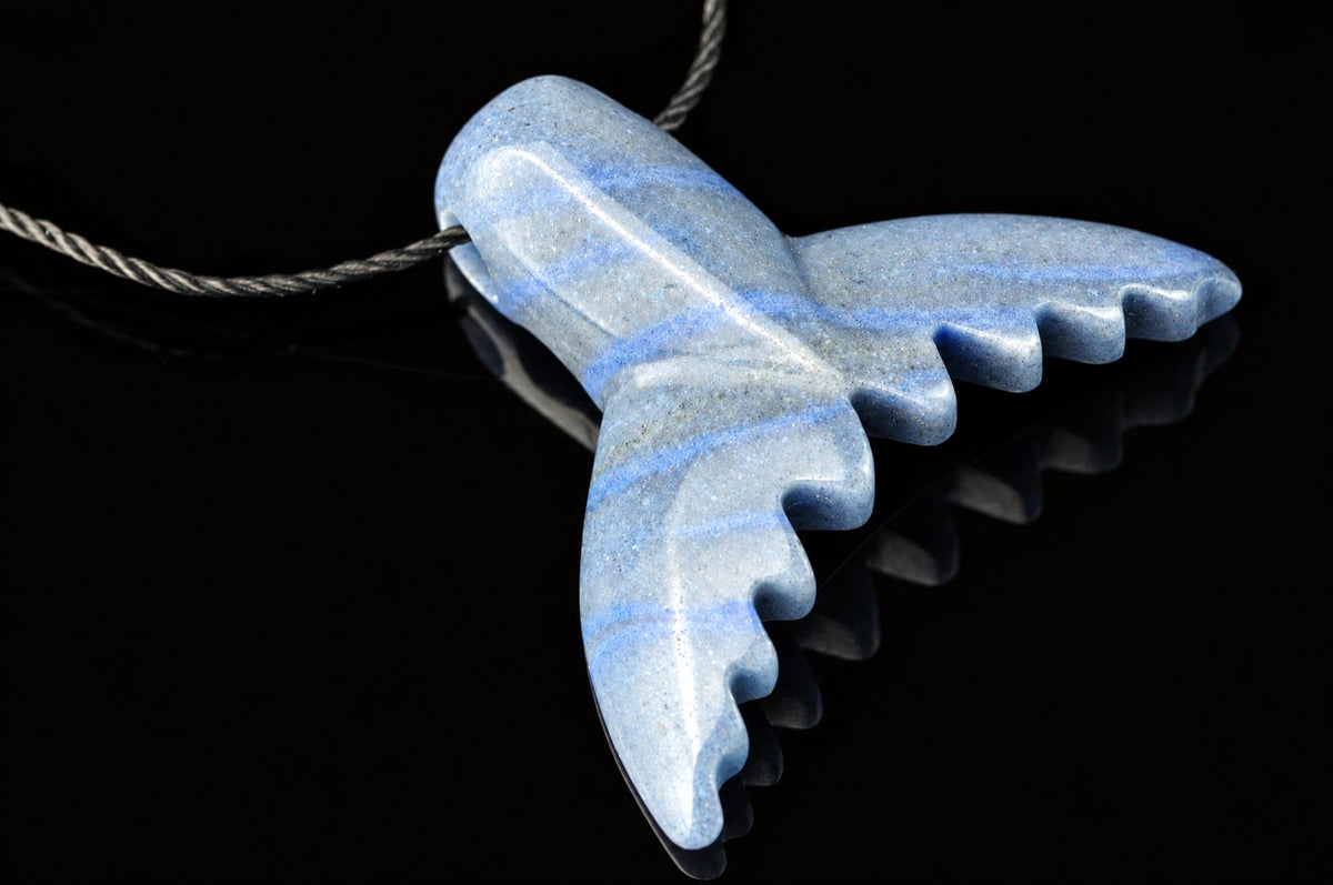 A polished blue quartz pendant shaped like a dolphin tail, with light blue stripes and a dark surface.