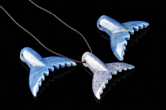 Three blue and white speckled dolphin-tail pendants on a dark surface, one attached to a twisted cord.