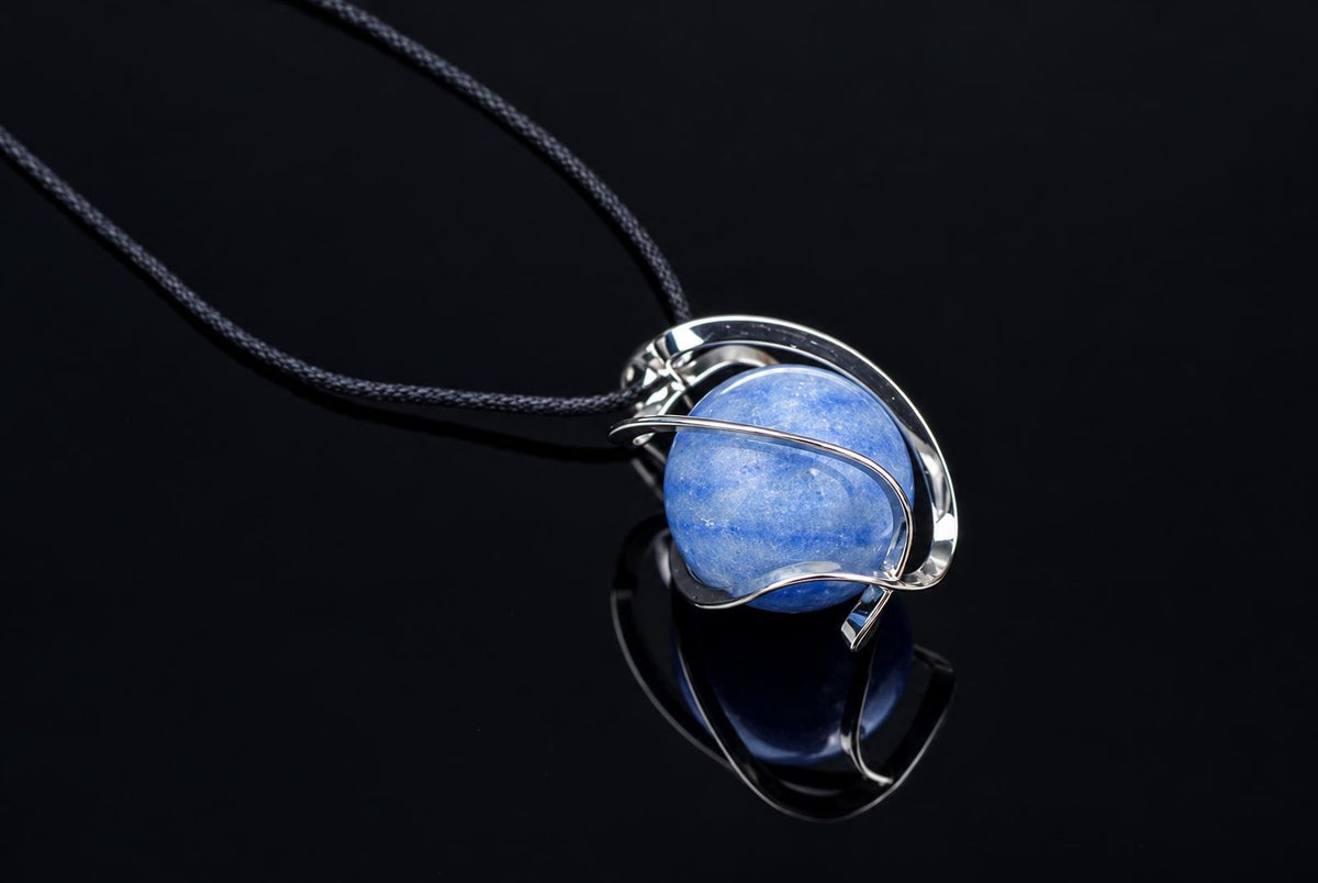 A blue quartz sphere pendant wrapped in silver-toned wire, on a dark cord against a black reflective surface.
