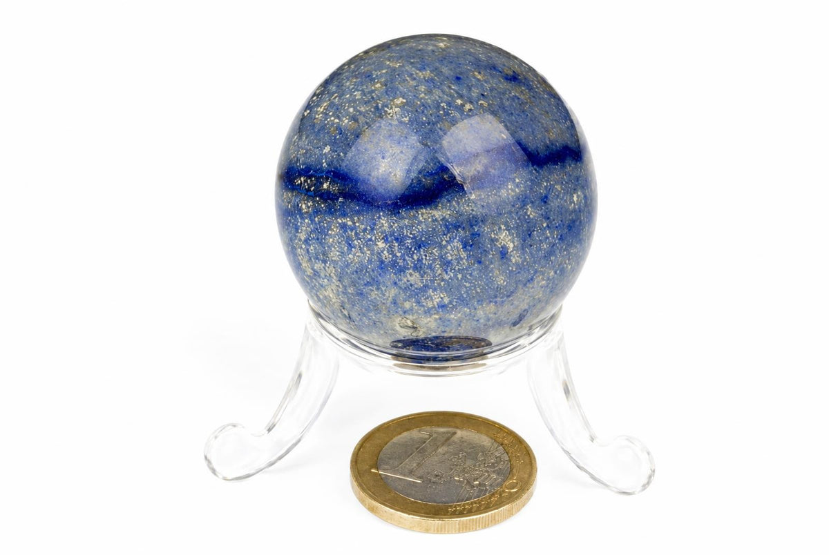 A polished blue quartz sphere with darker bands rests on a clear stand beside a coin on a white background.
