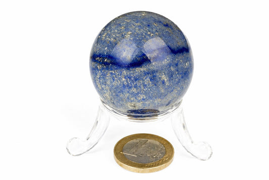 A polished blue quartz sphere with darker bands rests on a clear stand beside a coin on a white background.
