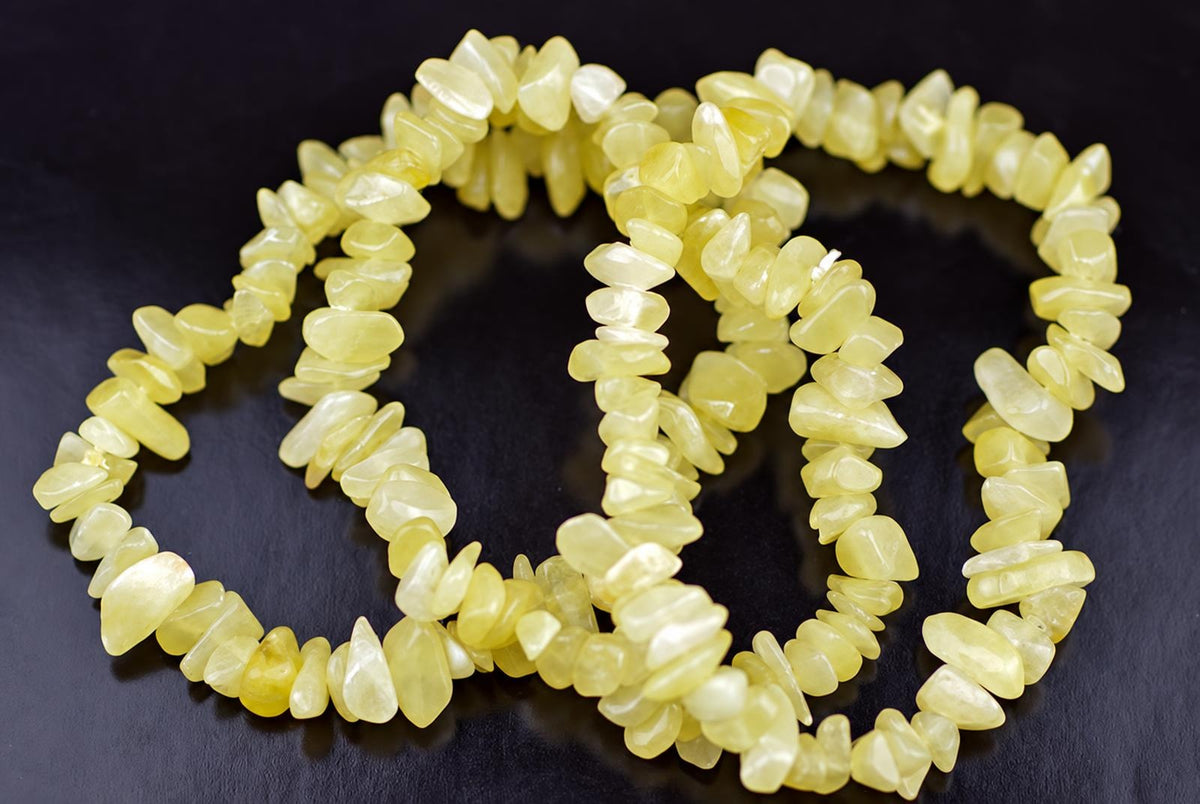 A yellow calcite chip bracelet coiled on a dark surface, showing irregular stone beads strung together.