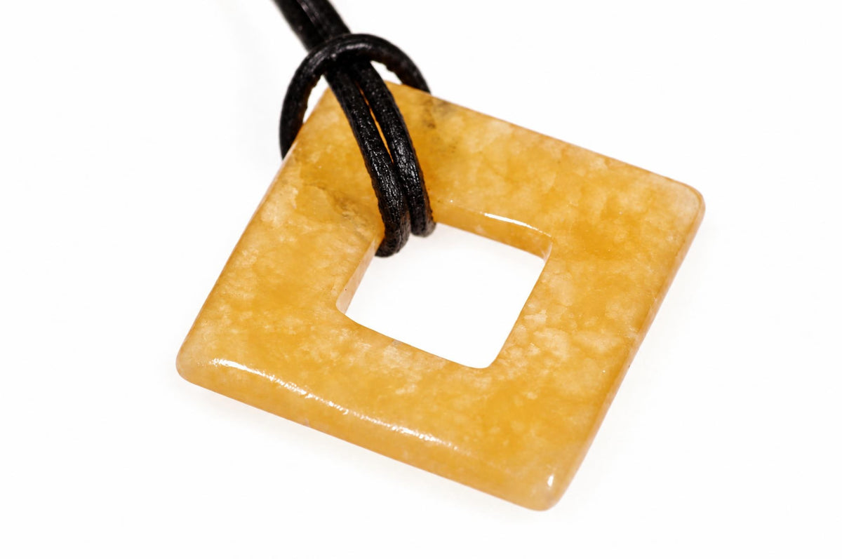 A square, donut-shaped pendant in yellowish calcite with a central hole, threaded on a black cord against a white background.