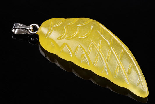 A yellow calcite pendant shaped like a wing, with carved vein details and a silver-toned bail, on a dark surface.