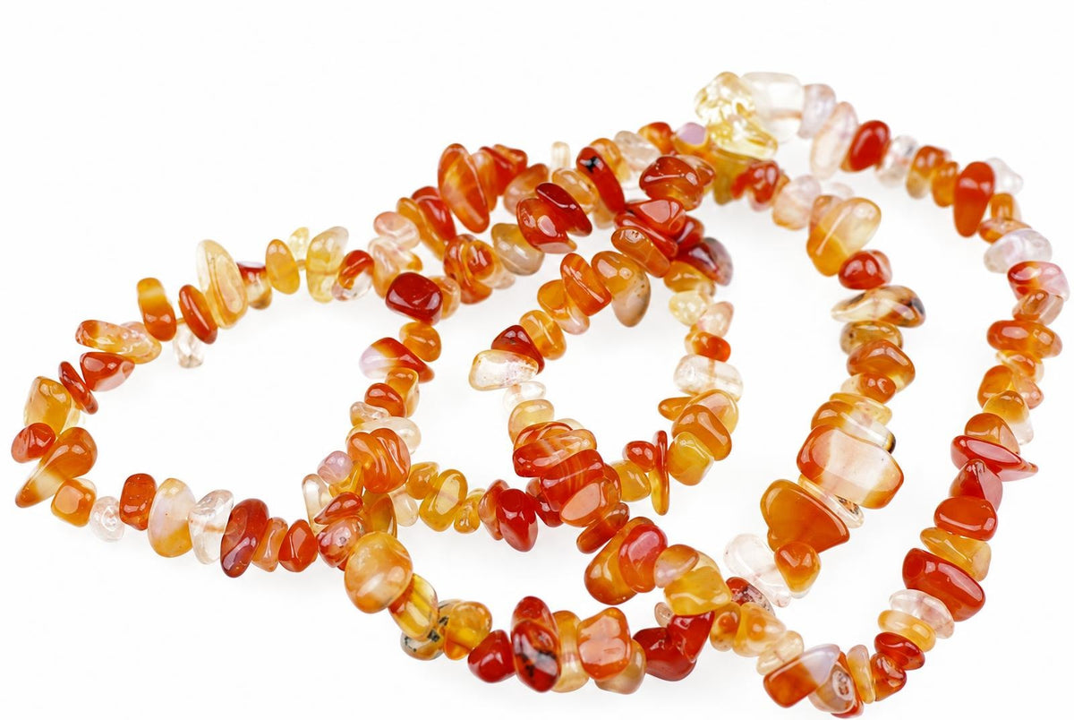 A necklace of irregular carnelian chips in red, orange, yellow and pale tones on a white surface.