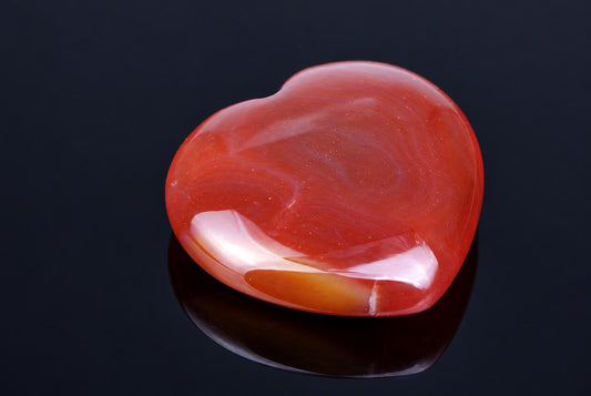 A polished, heart-shaped carnelian stone with red and white swirls rests on a dark surface.
