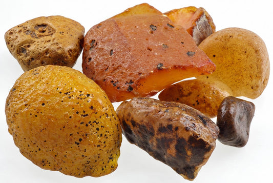 A group of natural carnelian stones in various shades of orange, yellow and brown with dark spots on a white surface.