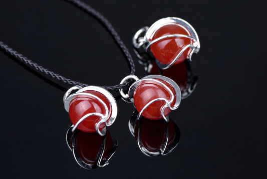 Three red spherical pendants with silver-toned wire wrapping on a dark cord, resting on a reflective black surface.