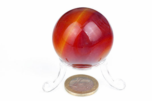 A polished red and orange striped sphere on a clear stand, with a coin for scale against a white background.
