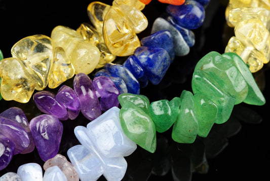 A close-up of a chakras bracelet with chips in yellow, blue, purple, green and white stones on a dark surface.