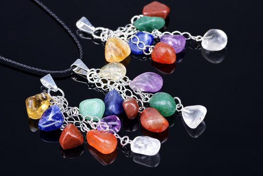 Pendant necklaces with clusters of colourful polished stones and silver-toned chain links lie on a dark reflective surface.