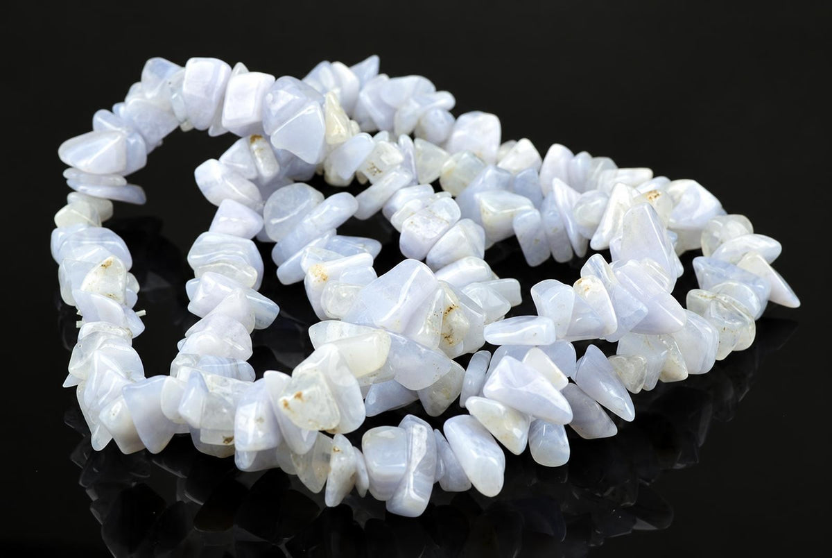 A bracelet made of irregular, polished chalcedony chips in pale blue and white tones arranged on a dark reflective surface.