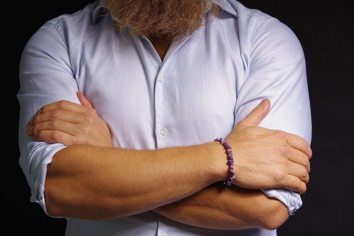 Man wearing a Charoite bracelet – Chips with crossed arms, featuring natural purple gemstone chips on his wrist against a white shirt and dark background.