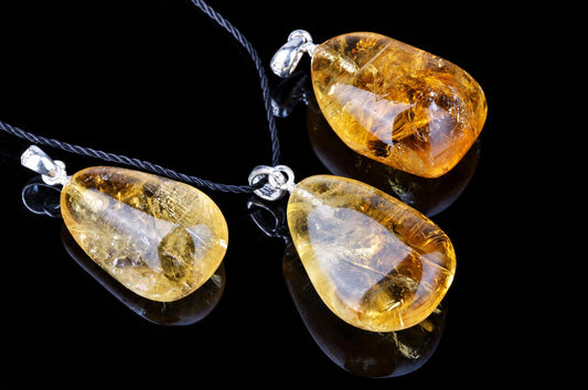 Polished golden-yellow citrine pendants on black cords lie on a dark reflective surface.