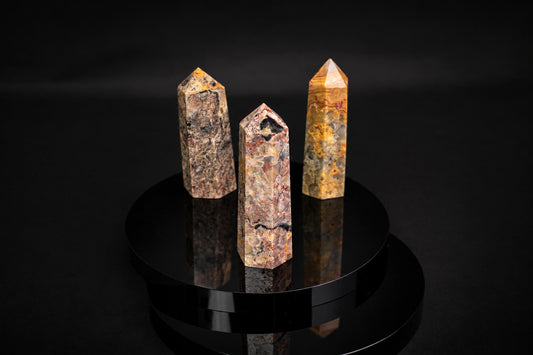 Three polished, pointed agate obelisks with varied brown, yellow and black patterns stand on a dark reflective surface.