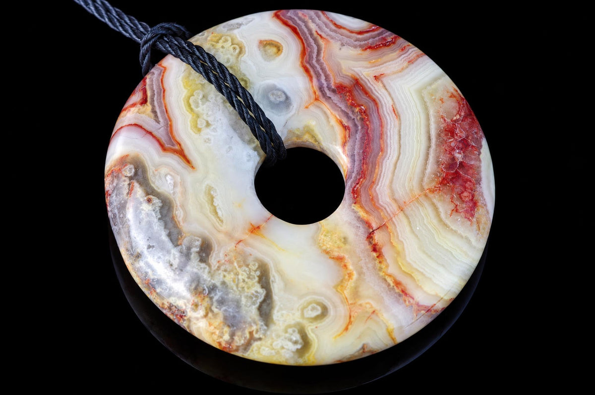 A polished donut-shaped pendant with swirling bands of white, red, yellow and grey agate on a dark surface.