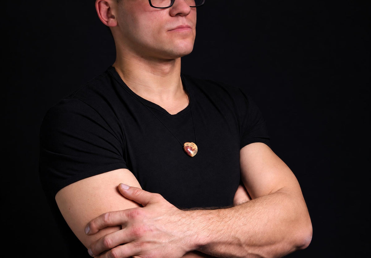 A man in a black t-shirt wears a heart-shaped pendant with brown and cream swirls on a dark surface.