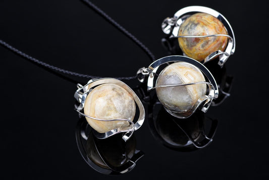 Three pendants with polished, banded agate spheres held in silver-toned wire frames on dark cords against a black reflective surface.