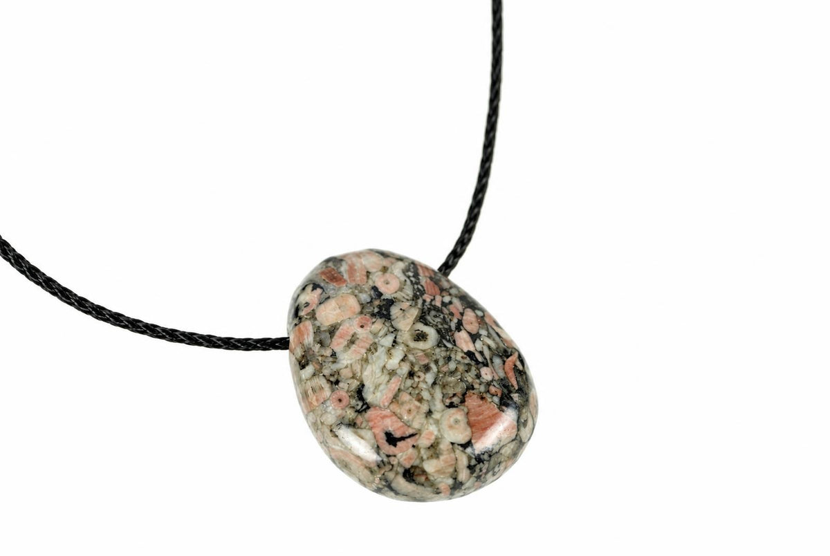 A polished oval pendant with pink, white and dark speckled stone on a black cord against a white background.
