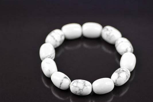Howlite bracelet with rounded white beads and grey veining arranged in a ring on a dark reflective surface, viewed at an angle with the front beads in focus.
