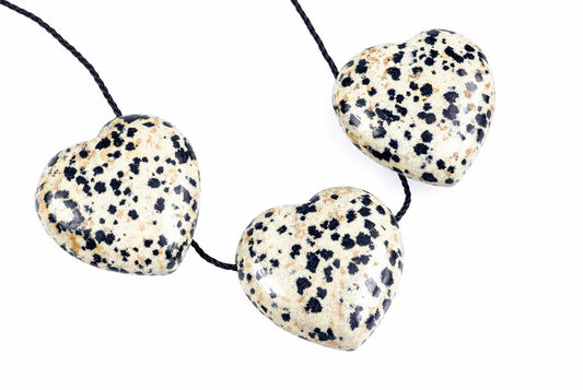 Three heart-shaped Dalmatian jasper pendants with black and tan spots on a cream background, strung on dark cord against white.