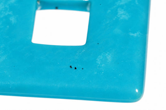 Close-up of a blue-green square pendant showing its central square opening and rounded edge against a white background.