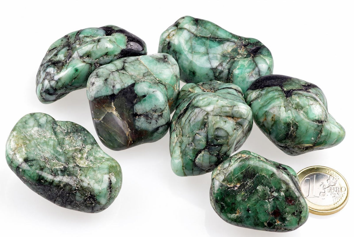 Seven polished green and black stones with white veining on a pale surface, next to a one euro coin.