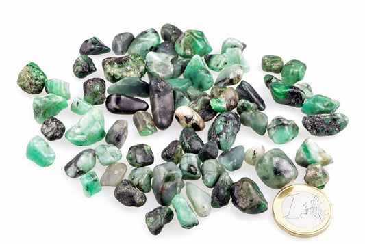 A pile of small, rough green stones with black and white inclusions on a white surface next to a one euro coin.