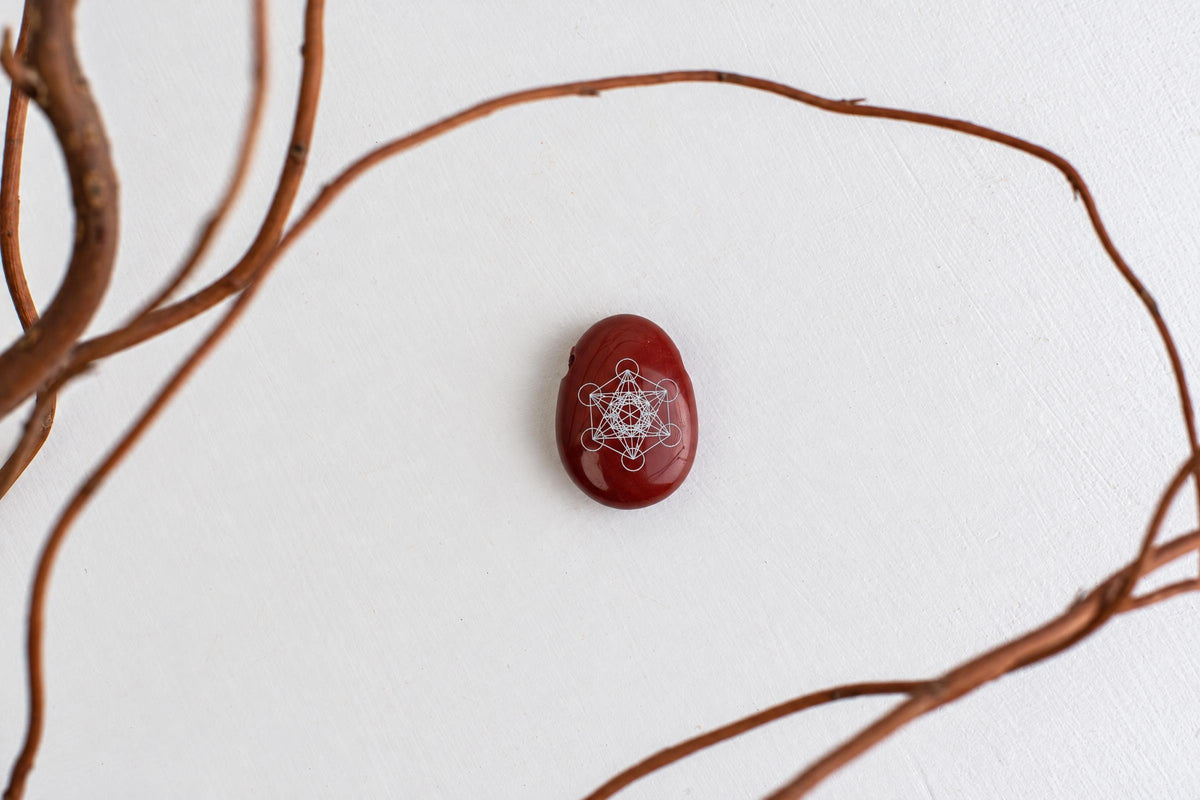 A polished dark red stone with a white geometric engraving, resting on a pale surface surrounded by brown twigs.