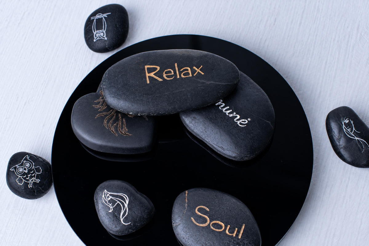 Black polished stones engraved with words and simple drawings are arranged on a round black tray, with smaller stones beside it.
