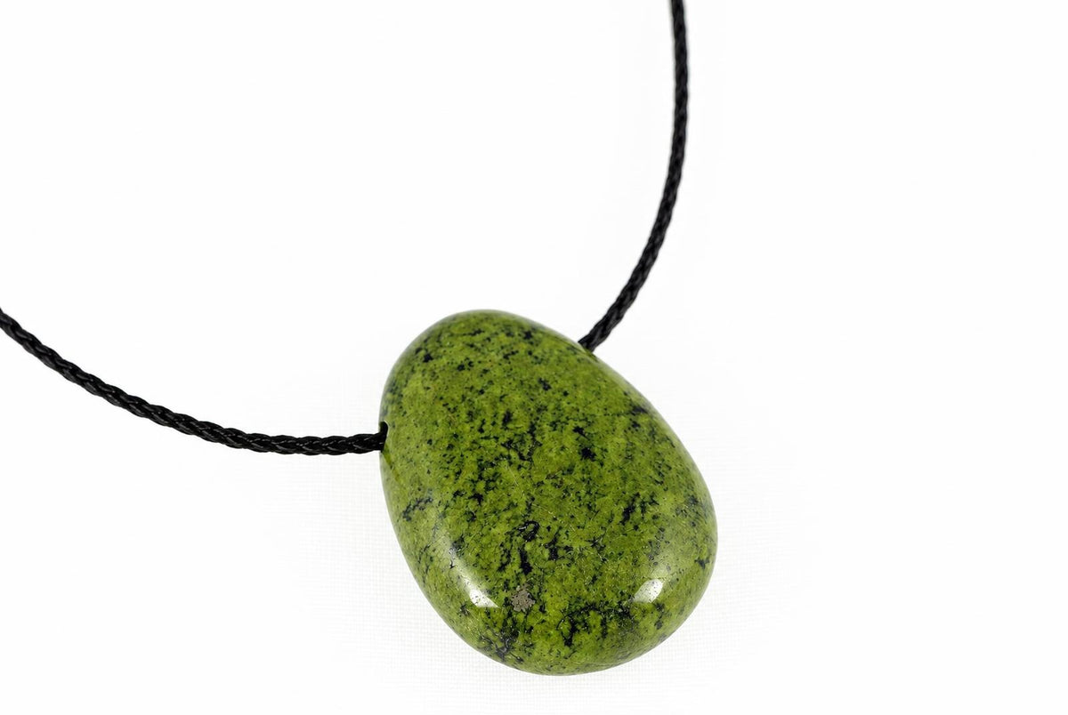 A polished green pendant with black speckles hangs from a dark cord against a white background.