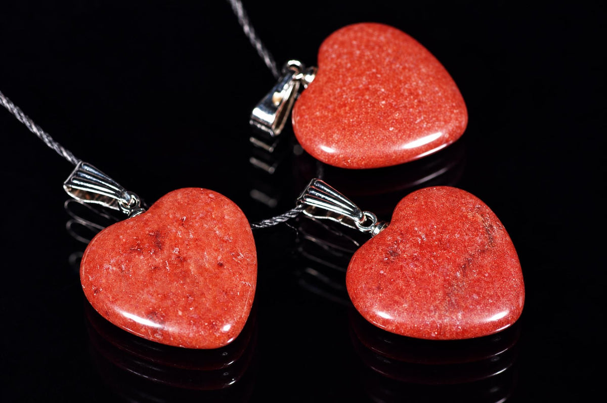 Polished red heart-shaped pendants on black cords lie on a dark reflective surface.