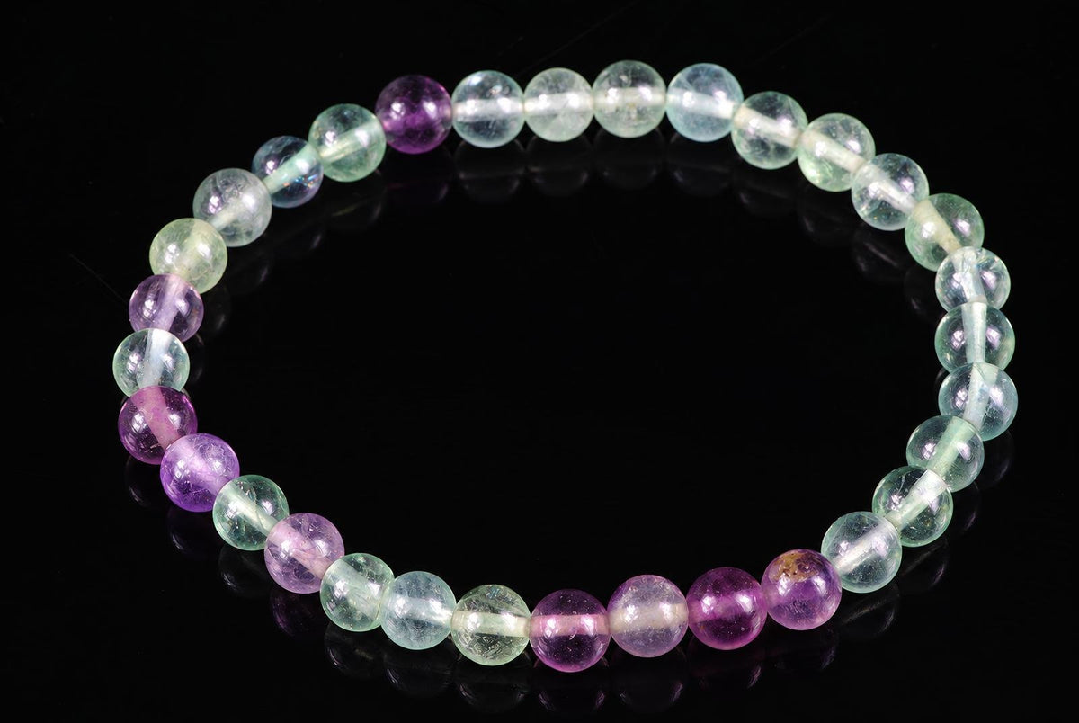 A bracelet of round beads in pale green, clear and purple tones on a dark surface.