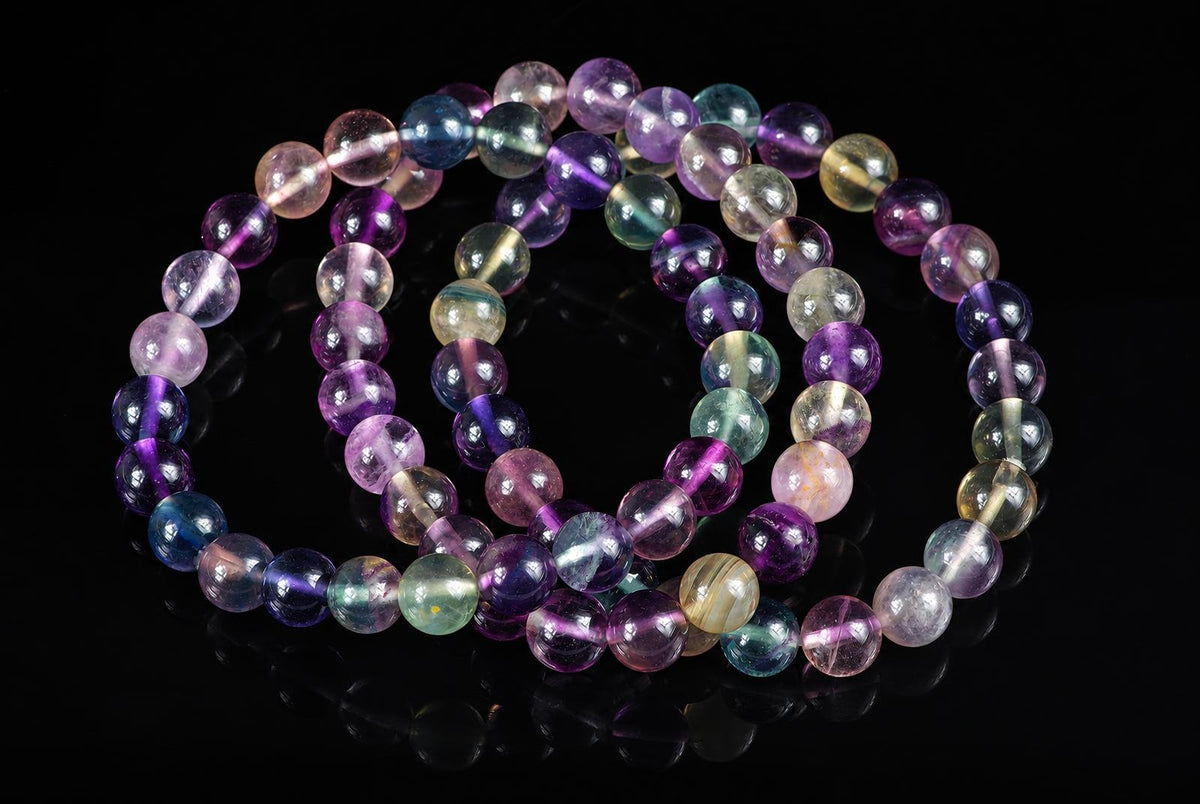A Fluorite bracelet with round beads in purple, blue, green and yellow tones on a dark surface.