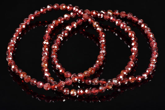 A faceted red garnet bracelet with multiple strands of round beads arranged in a coil on a dark reflective surface.