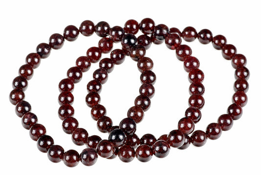 A strand of round, dark red garnet beads arranged in a loose coil on a white surface.