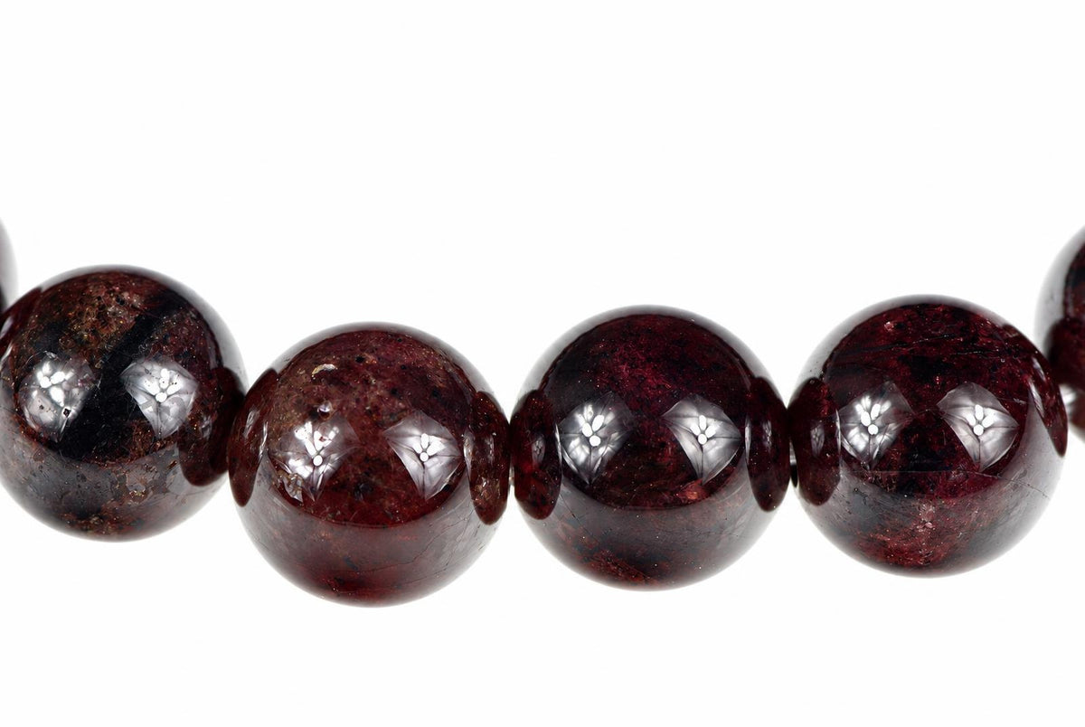 A row of round, polished beads in dark red and black with silver-toned reflections on a white surface.