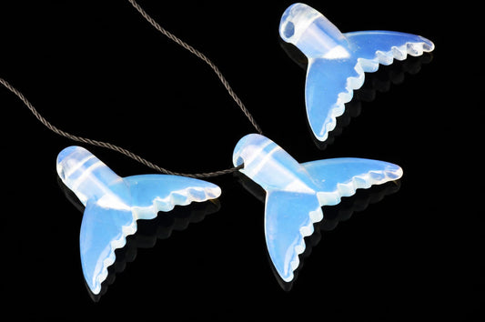 Three translucent blue dolphin-tail pendants on a dark cord, arranged diagonally on a black reflective surface.