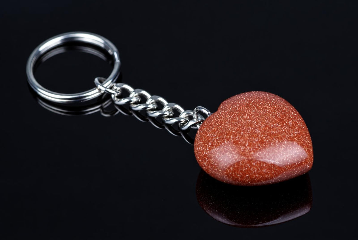 A silver-toned keychain with a heart-shaped goldstone pendant on a dark reflective surface.